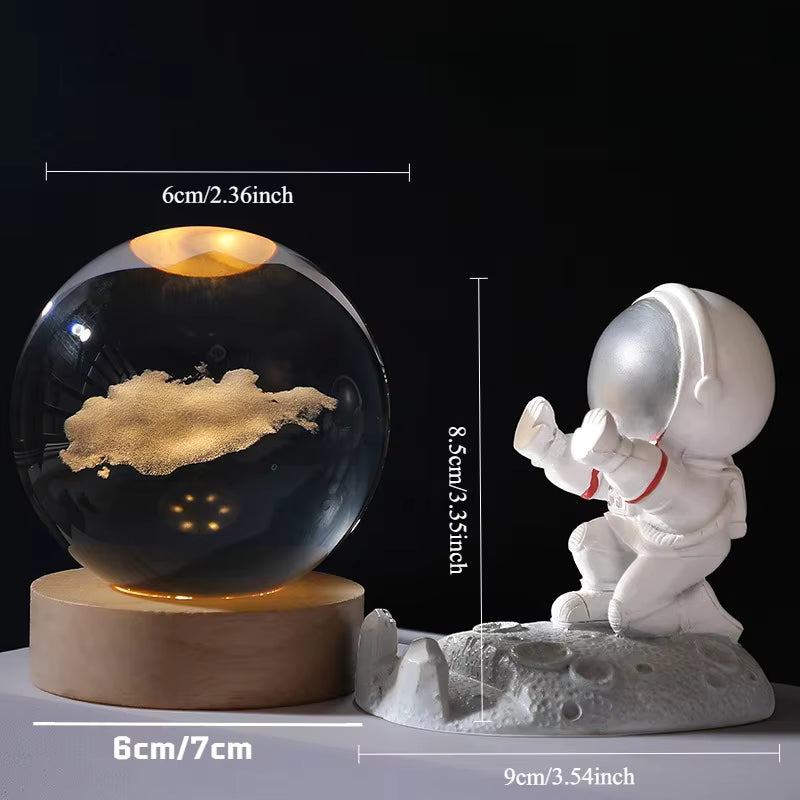 A space-themed desk lamp set shown with dimension labels: a large black globe containing a glowing gold cloud and warm light on a round wooden base, next to a white astronaut figurine on a gray moon-like base. The image includes measurements for width, height, and depth.